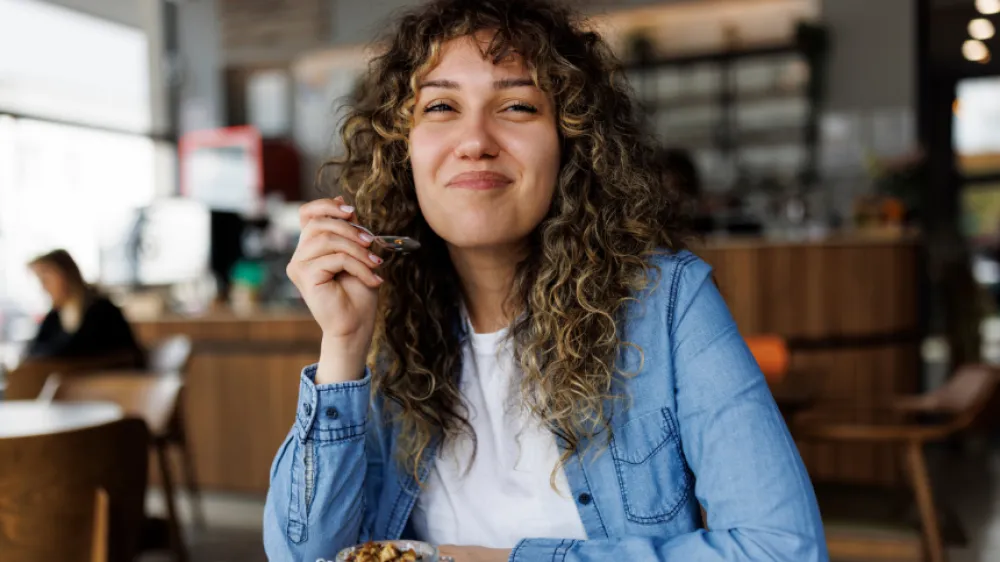 Hero - A smiling young woman eating chia pudding for breakfast at cafe