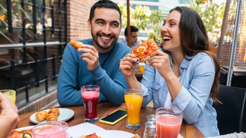Hero A Caucasian man and woman sitting at an outdoor table eating pizza and enjoying time with frien
