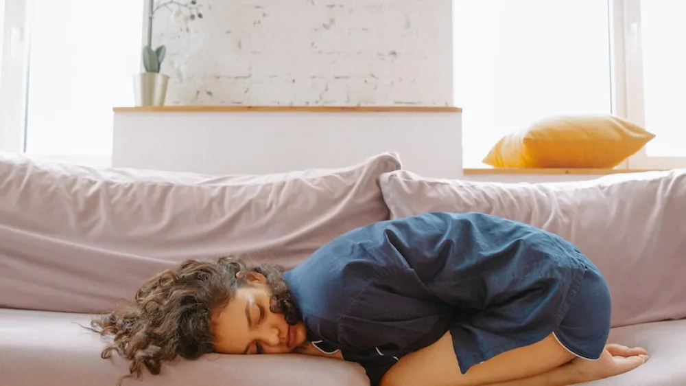 Young girl holding her stomach in pain on couch 860x484